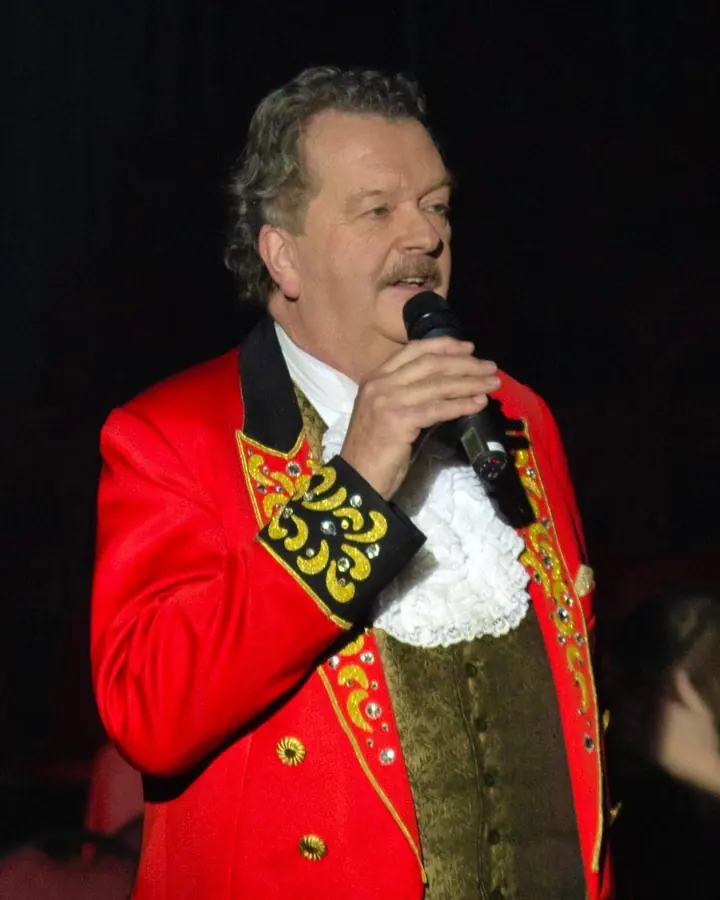 Spreekstalmeester Robert Ronday in rood rokkostuum met microfoon