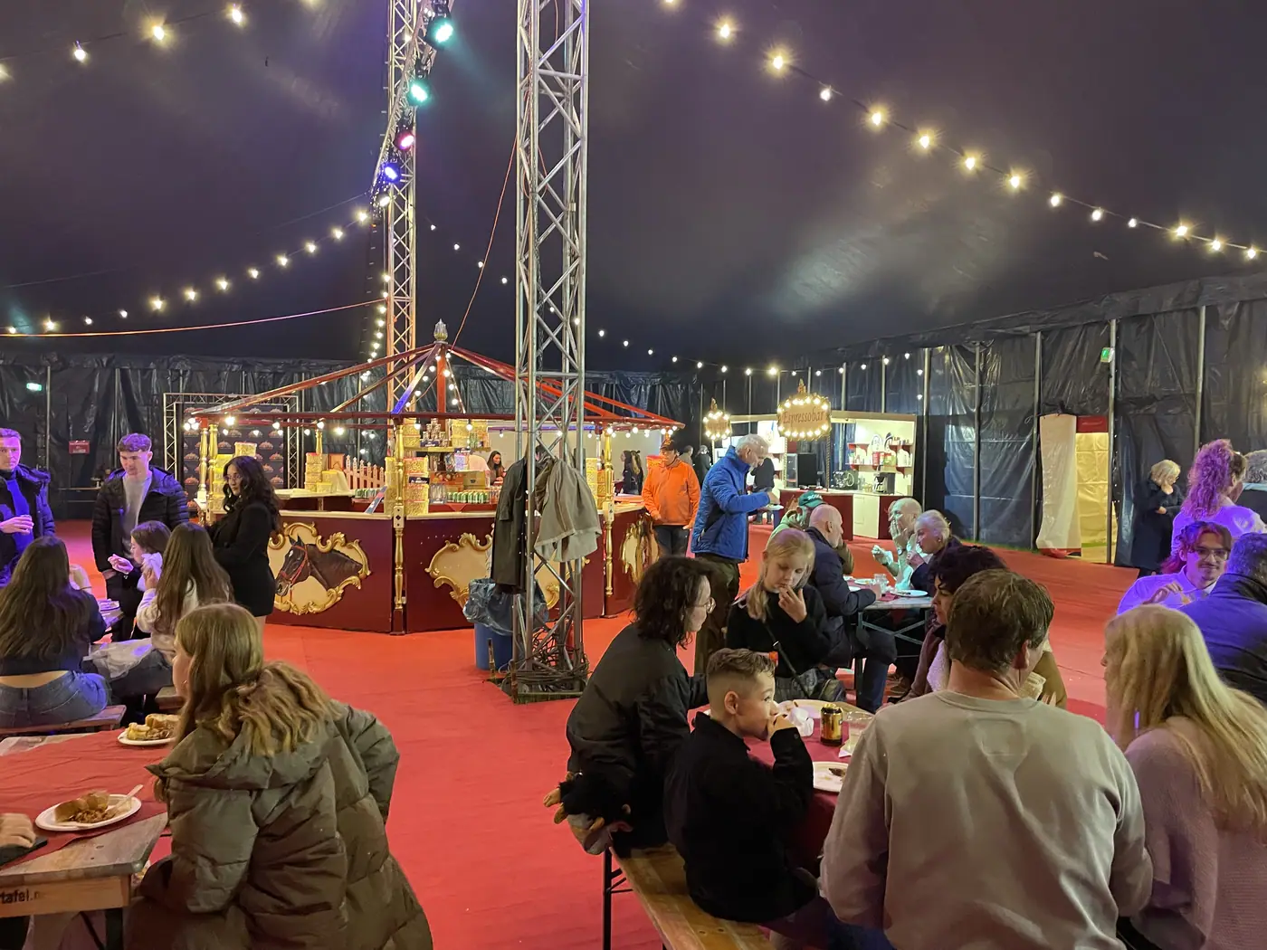 Bezoekers aan de tafels in de foyertent onder slingers van lampjes
